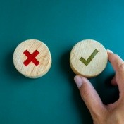 person holding wooden circle with checkmark and a X